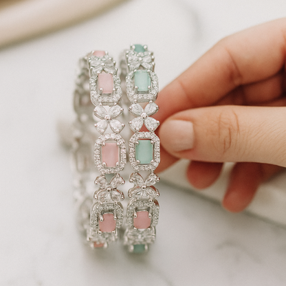Hand holding a pair of decorative bracelets with pastel stones on a marble. Brand: Oplique By Vineetasurface