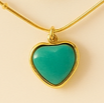 Turquoise heart-shaped pendant on a gold chain against a beige background. Brand: Oplique By Vineeta
